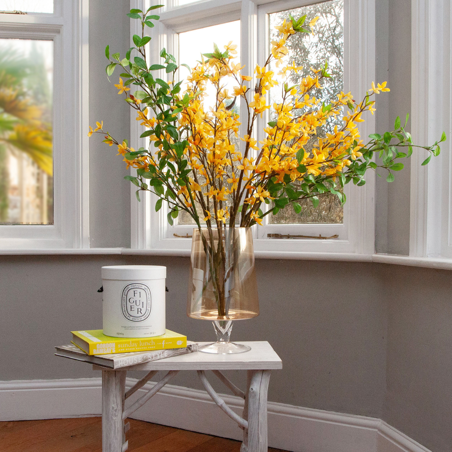 Artificial forsythia arrangement with bright yellow spring blossoms displayed in a footed amber glass vase
