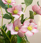 Artficial hellebore flowers arranged in a moss pot with foliage and willow