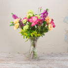 Artificial rose and stock summer flower arrangement in a clear grand waisted glass vase