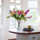 Artificial rose and stock summer flower arrangement in a clear grand waisted glass vase