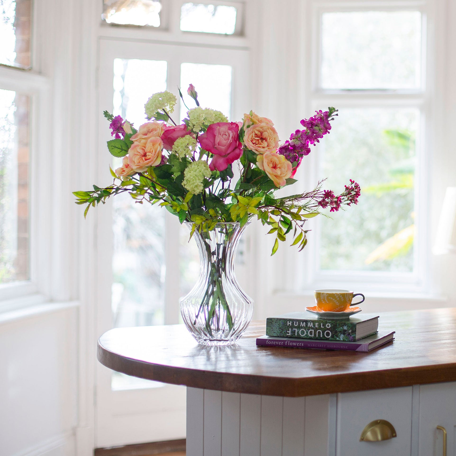 Artificial rose and stock summer flower arrangement in a clear grand waisted glass vase