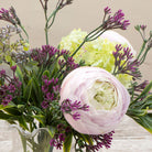 Artificial ranunculus and foliage arrangement in a clear glass garlic vase