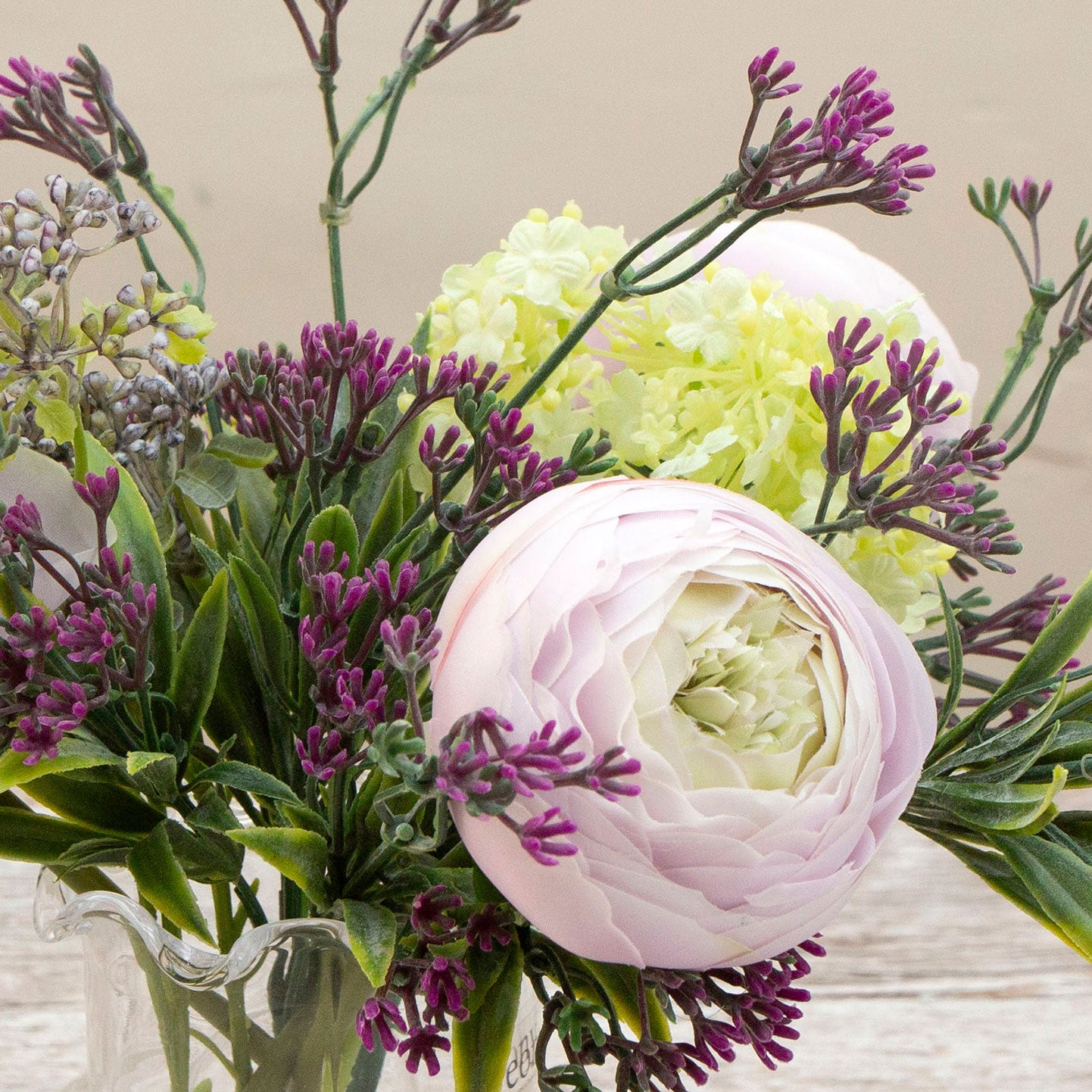 Artificial ranunculus and foliage arrangement in a clear glass garlic vase