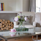 Artificial ranunculus and foliage arrangement in a clear glass garlic vase