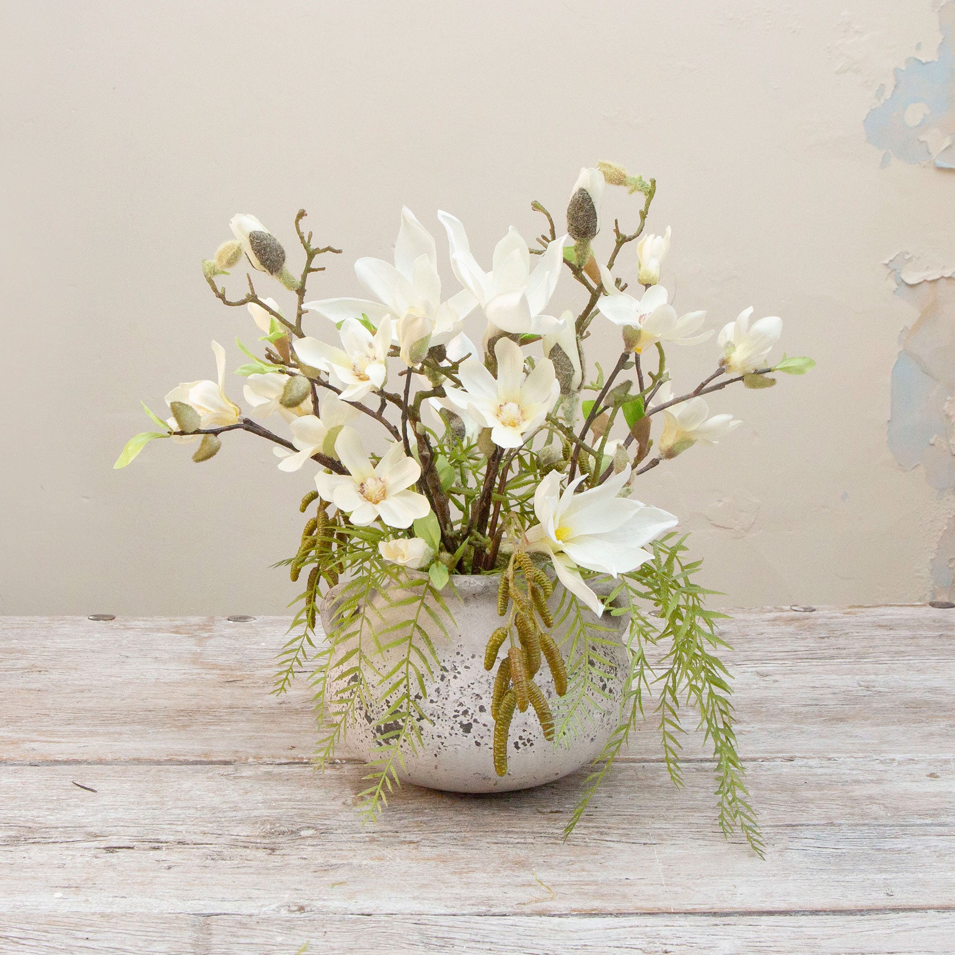 Artificial magnolia flowers arranged in a rustic grey handled planter with birch and willow