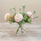 Artificial ranunculus and foliage arrangement in a clear glass garlic vase