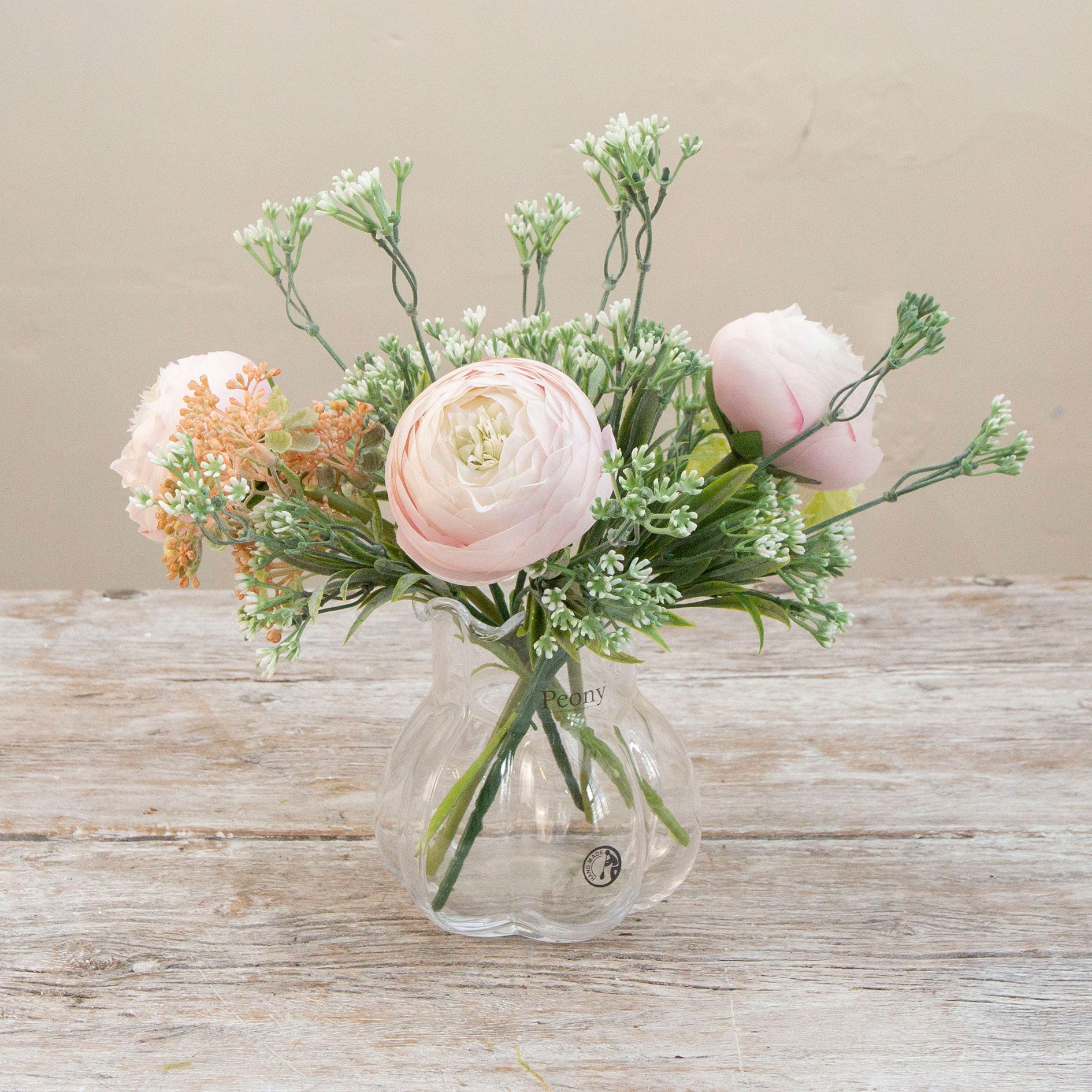 Artificial ranunculus and foliage arrangement in a clear glass garlic vase