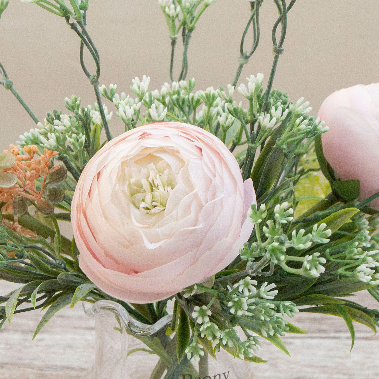 Artificial ranunculus and foliage arrangement in a clear glass garlic vase