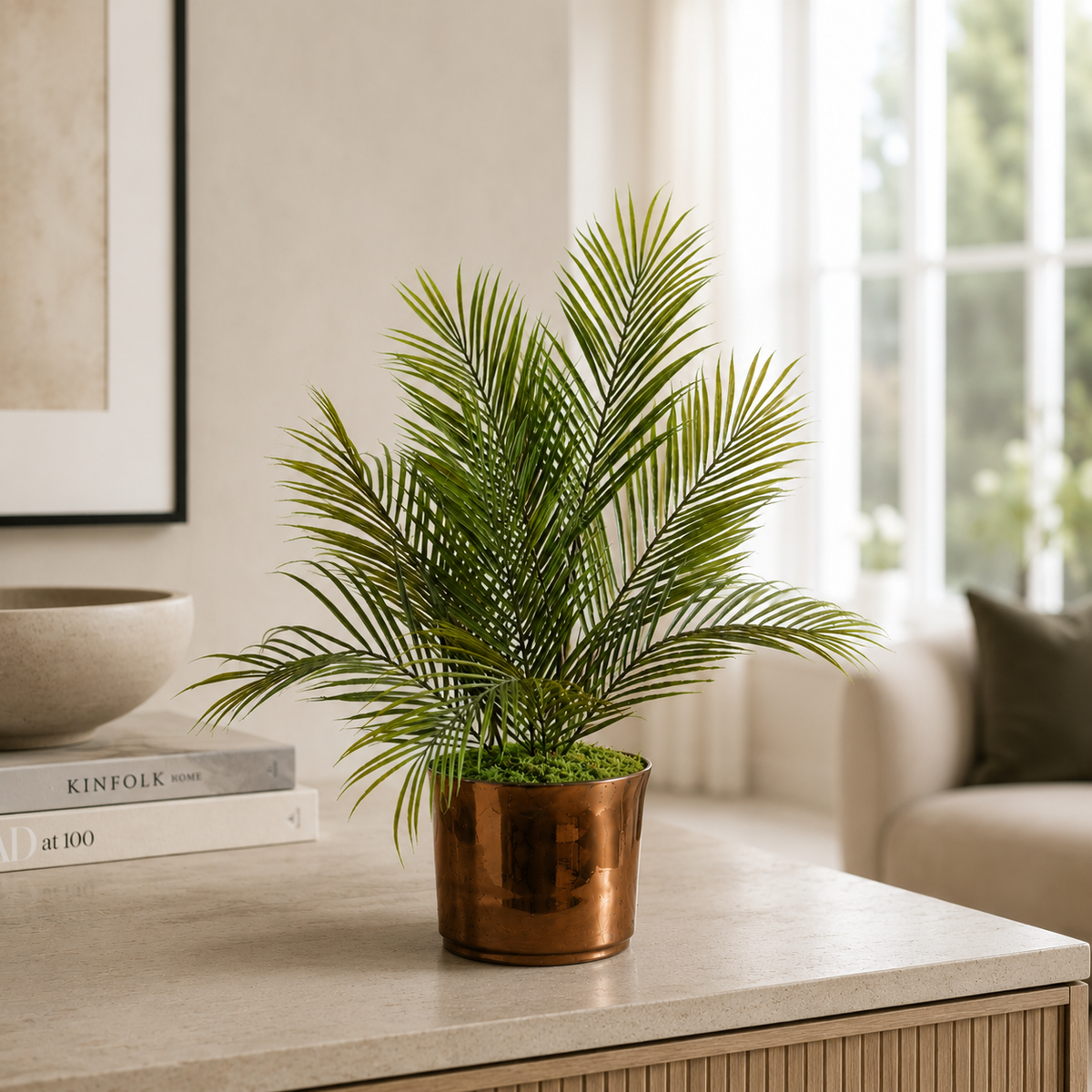 Artificial areca palm with realistic green fronds in a gold ceramic pot, styled on a console table in a neutral living room