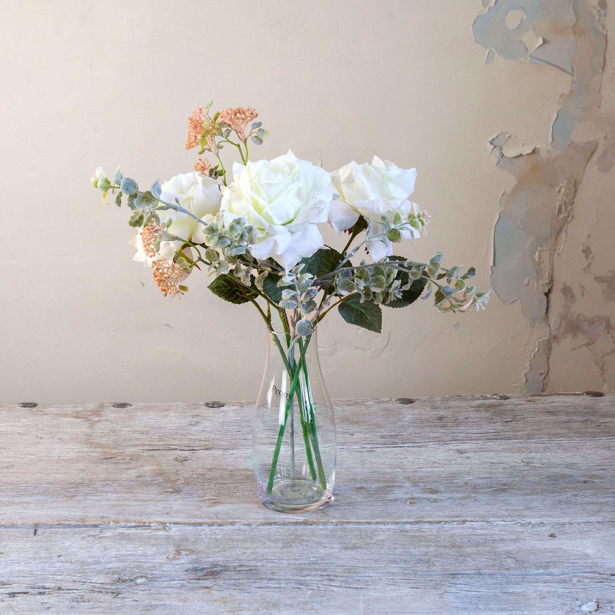 Artificial white roses and patrinia set in a clear glass milk bottle vase.