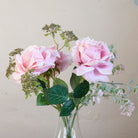 Close-up of artificial pink roses and patrinia set in a clear glass milk bottle vase.