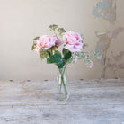 Artificial pink roses and patrinia set in a clear glass milk bottle vase