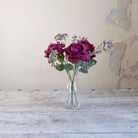 Artificial burgundy roses and patrinia arrangement  in a clear glass milk bottle vase.