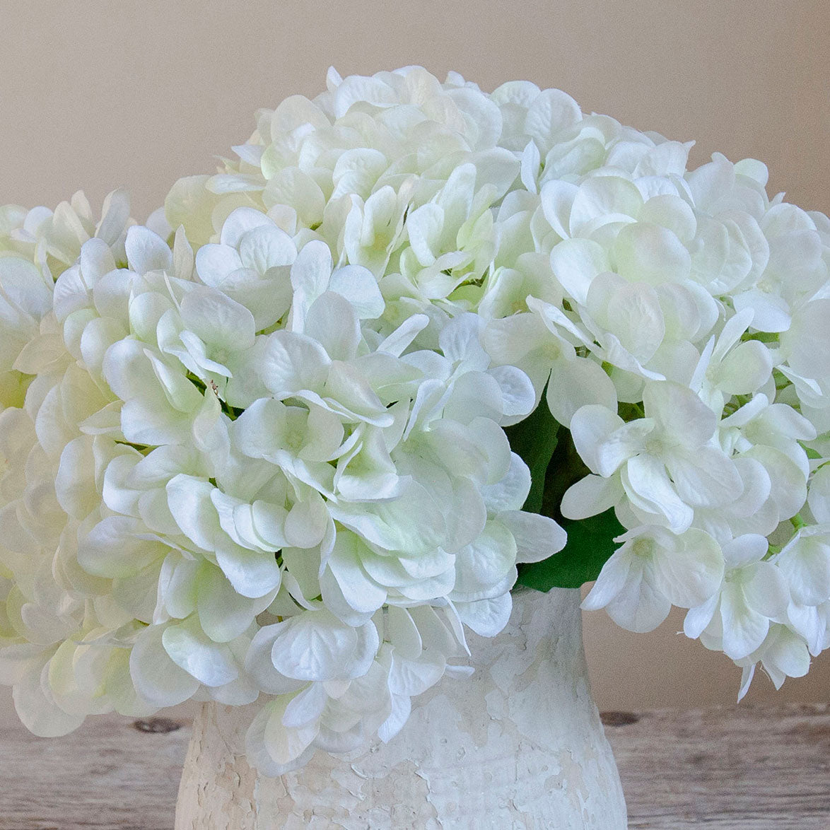 Close-up of lifelike artificial white hydrangea blooms in a rustic textured white pot.