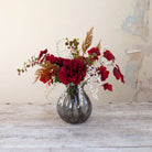 Artificial Rose, Grape Leaf & Acacia Arrangement with rich burgundy roses, red grape foliage, white acacia and warm autumnal accents in a smoked pumpkin glass vase