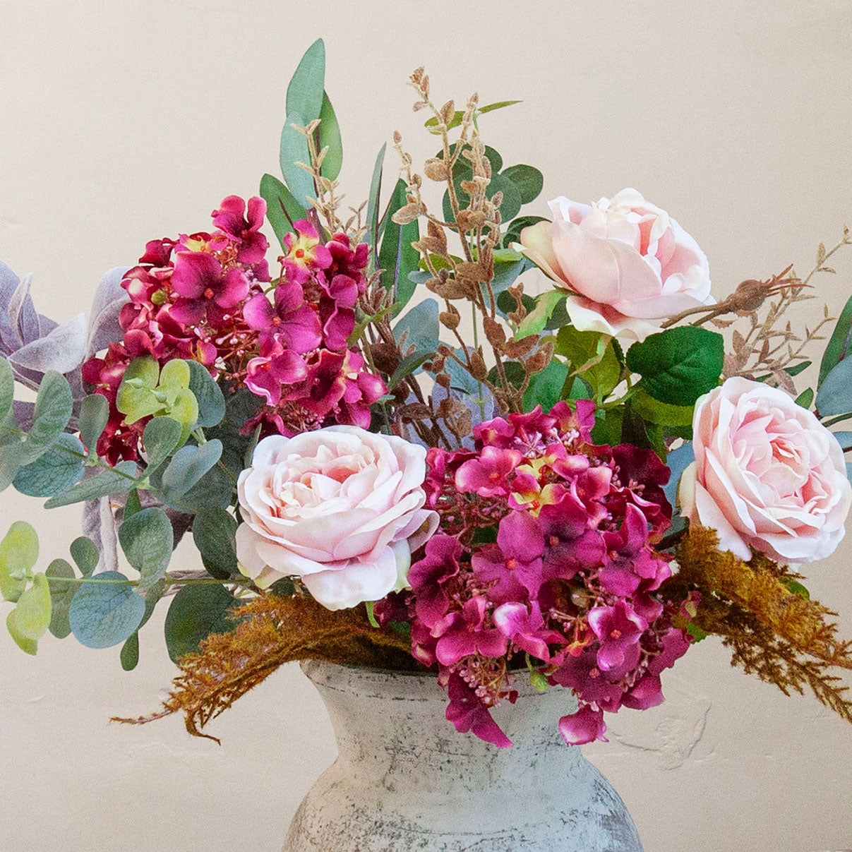 Close-up of artificial pink roses and rich burgundy hydrangeas with realistic eucalyptus and autumn foliage.
