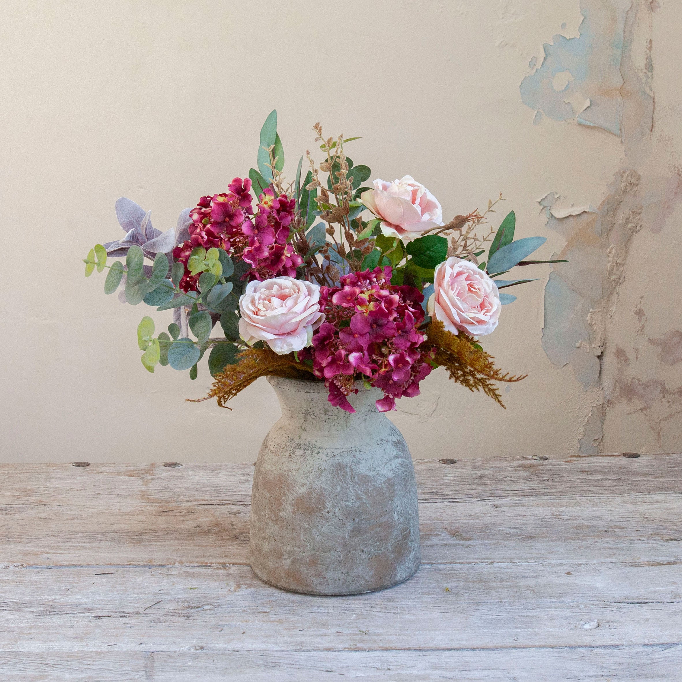 Artificial rose and hydrangea arrangement in soft pink, rich burgundy and muted foliage, arranged in a rustic stone-effect vase