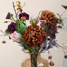 Close up of artificial chrysanthemum, rose and foliage bouquet in warm autumn tones, displayed in an amber glass vase.