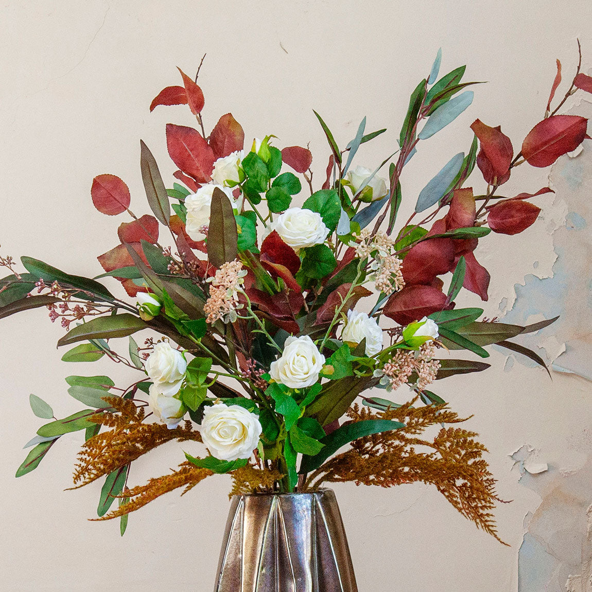 Close-up of an artificial rose and berry arrangement with white roses and rich autumn foliage in a tall bronze geometric pot.
