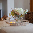 Close-up of artificial white hydrangea and ranunculus flowers with realistic autumn foliage in a clear glass rope lantern vase