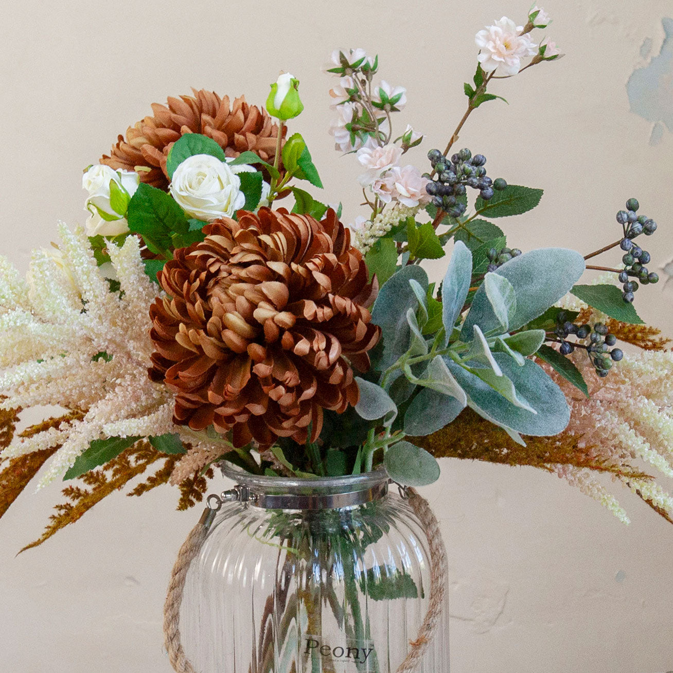 Close up of artificial chrysanthemum, rose and astilbe bouquet in warm autumn tones, displayed in a clear glass rope vase available separately.