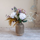 Artificial dahlia, hydrangea and thistle bouquet in soft white, blush and muted autumn tones, displayed in a textured bronze vase.
