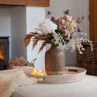 Artificial dahlia, hydrangea and thistle bouquet in soft white, blush and muted autumn tones, styled in a textured bronze vase in a cosy living room.