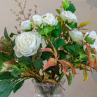 Close-up of artificial white roses and ranunculus with realistic green and warm autumn foliage.