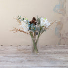 Artificial Amaryllis, Pine Cone & Eucalyptus Arrangement with white amaryllis blooms, brown pine cones, frosted winter foliage and eucalyptus  in a textured clear cylinder glass vase