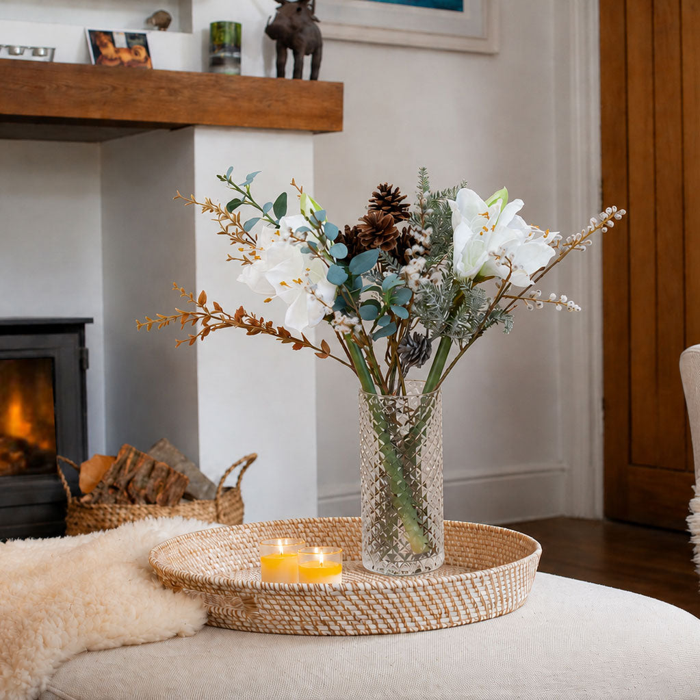 Lifestyle photo of Artificial Amaryllis, Pine Cone & Eucalyptus Arrangement with white amaryllis blooms, brown pine cones, frosted winter foliage and eucalyptus in a textured clear cylinder glass vase