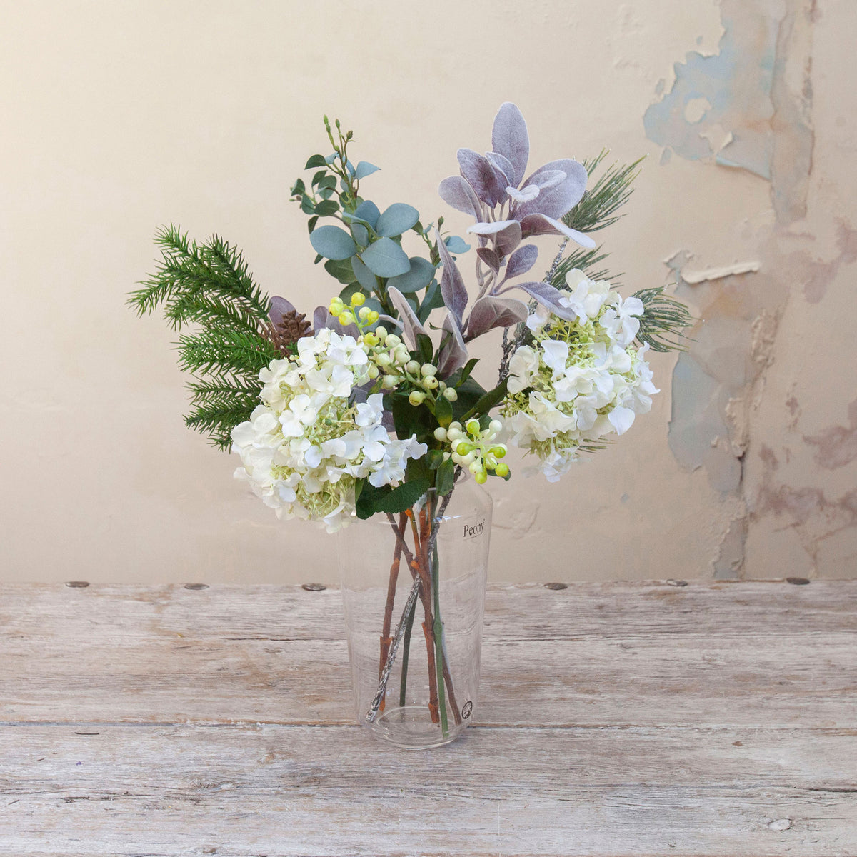 Artificial Seeded Hydrangea, Berries & Pine Cone Bouquet with white hydrangea blooms, green berries, eucalyptus, pine foliage and natural pine cone accents displayed in a clear glass vase