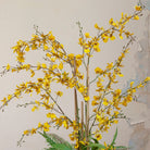 Close-up of artificial yellow dancing orchids with realistic branching stems and fern foliage.