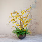 Artificial yellow Dancing Orchids with fern foliage arranged in a bronze footed bowl