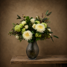 Artificial cream chrysanthemums, roses and green viburnum with botanical foliage and berries, arranged in a smoked ribbed optic glass vase.
