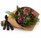 Artificial roses, hellebores and foliage in rich burgundy and pink tones, displayed as a hand-tied bouquet wrapped in brown kraft paper with a black satin ribbon.