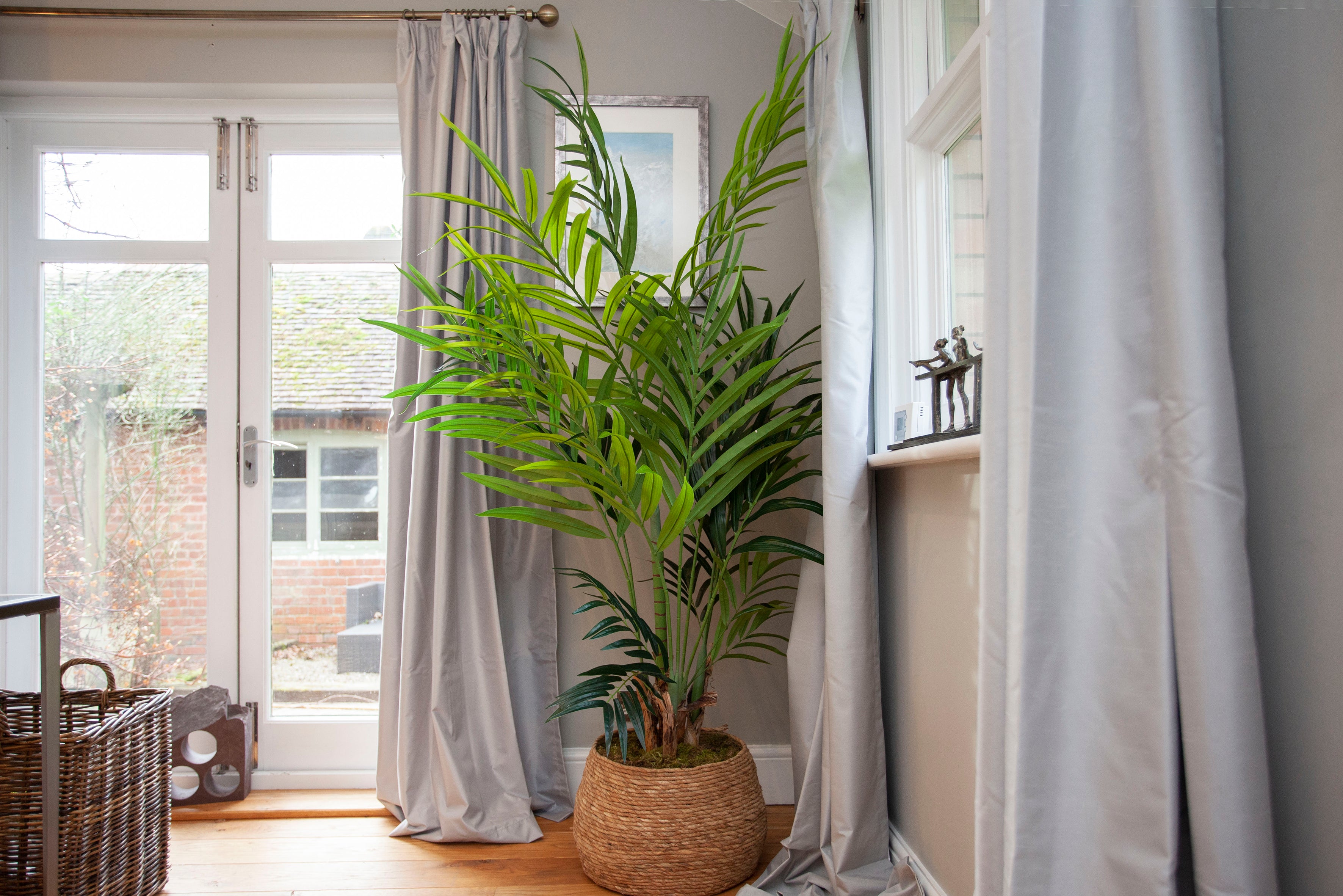 Artificial Kentia palm with lush green fronds and natural variation, planted with real moss and displayed in a hand-woven basket planter.
