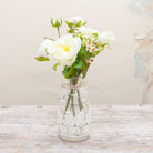 Roses & ranunculas with wax flowers in a lace bottle vase with ribbon trim Peony