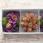 Close up view of the set of three decorative artificial  f hanging balls with pine cones and hydrangeas displayed against a wooden background.