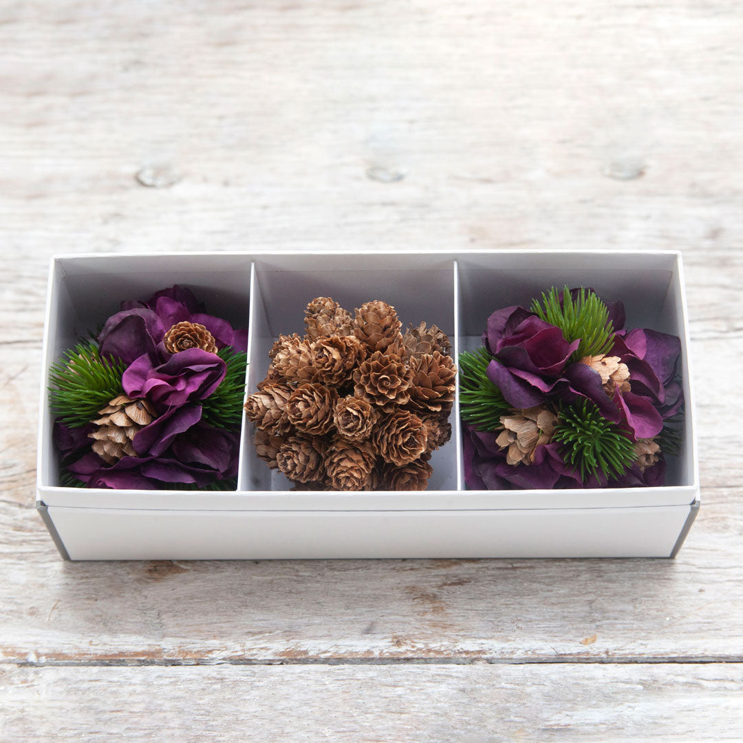 A set of three decorative artificial  hanging balls with pine cones and hydrangeas displayed against a wooden background.