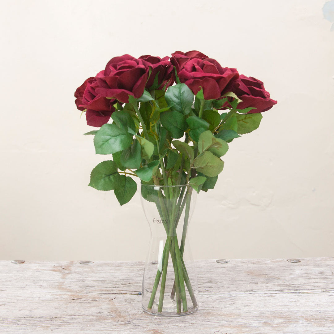 Artificial long stemmed red velvet Princess roses with green leaves, displayed in a clear glass vase