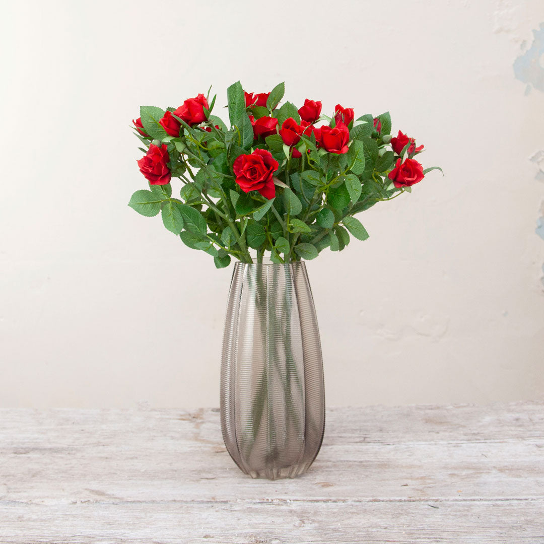 Artificial red rose stemS displayed in a smoked tall ridged glass vase for styling purposes only