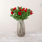 Artificial red rose stemS displayed in a smoked tall ridged glass vase for styling purposes only