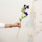 Artificial sweet pea stem being held in hand, featuring rich purple blooms with subtle purple-pink undertones on a slender green stem.