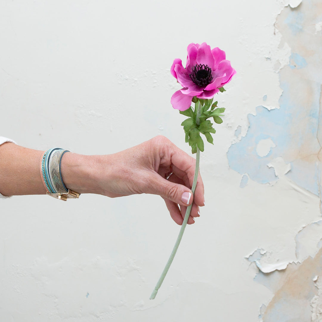 Hand holding artificial pink anemone with dark centre stem