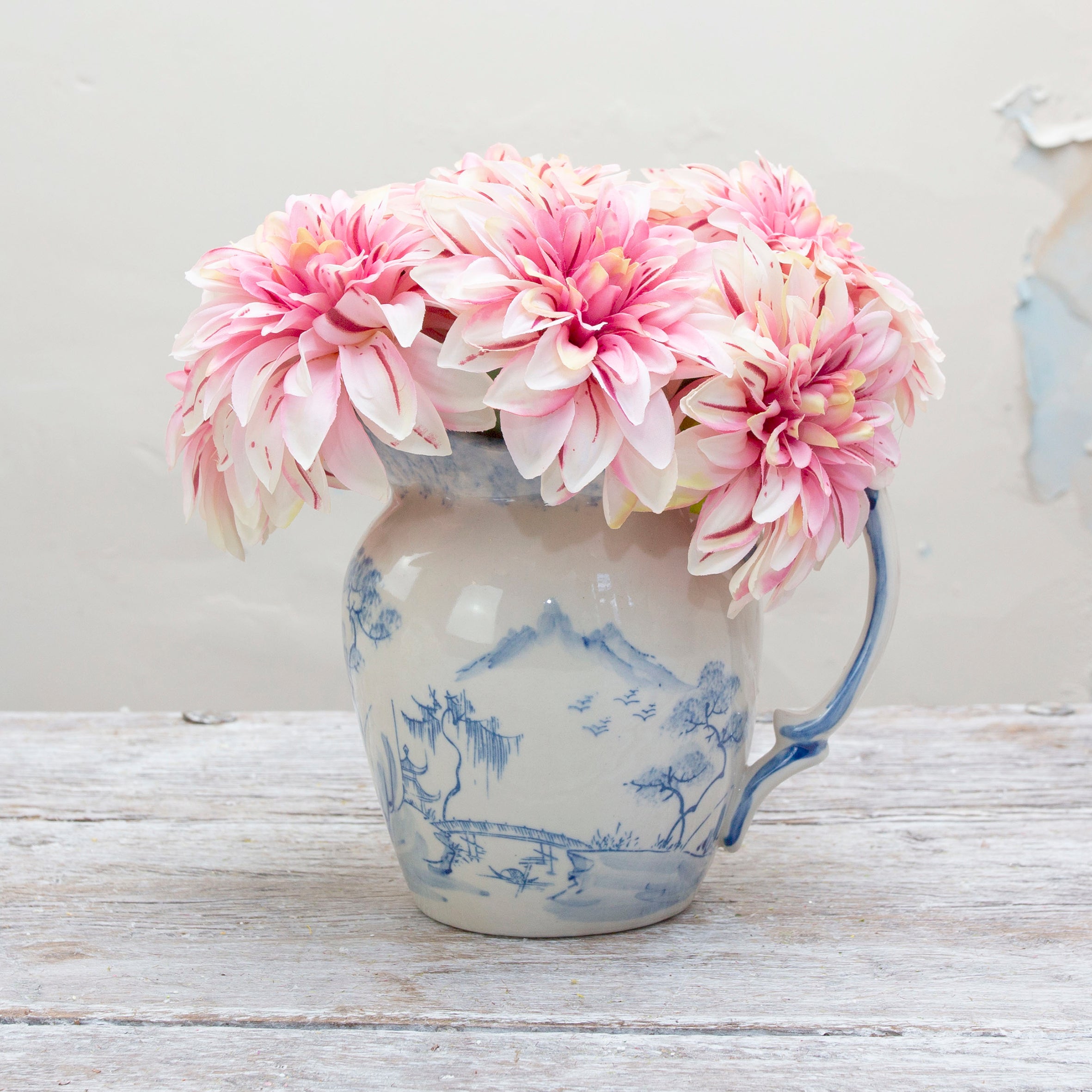 A bouquet of pink dahlia flowers with fuchsia stripes displayed in a blue and white ceramic jug.