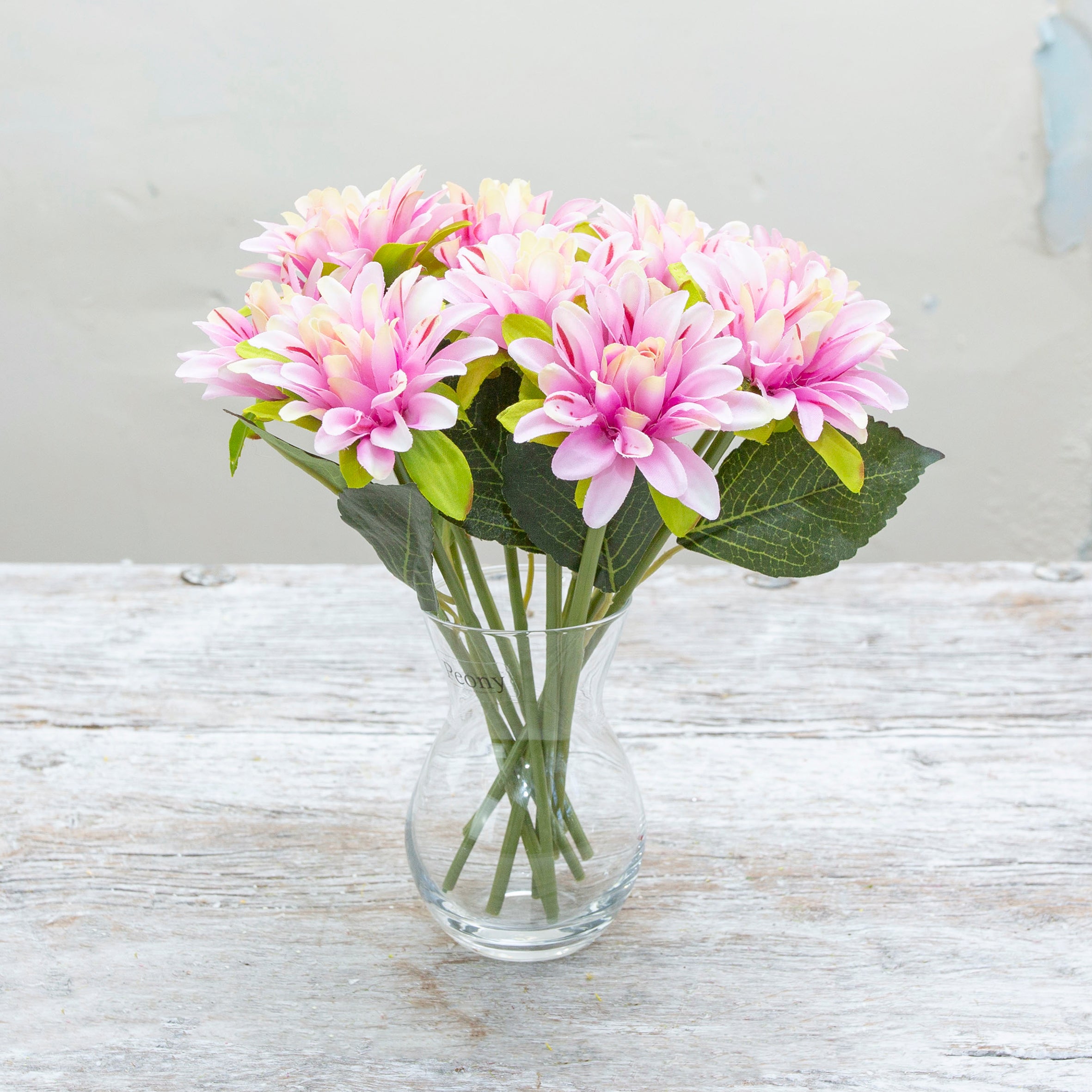 Artificial pink dahlia stems displayed in a glass vase
