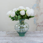 Artificial white peony stem displayed in a vase, showcasing a full, rounded bloom with lush green leaves for an elegant, timeless look.