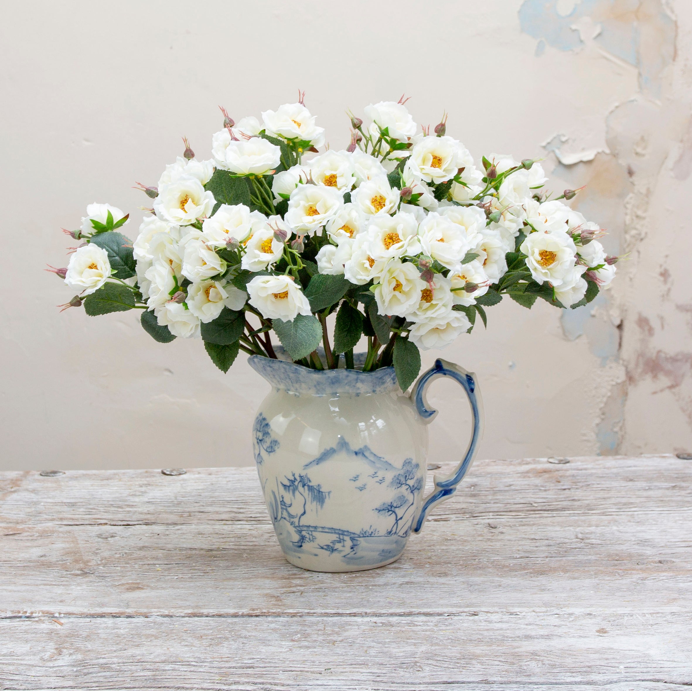 Artificial white rose spray stem displayed in a vase, showcasing softly opened white roses, layered petals and natural green leaves