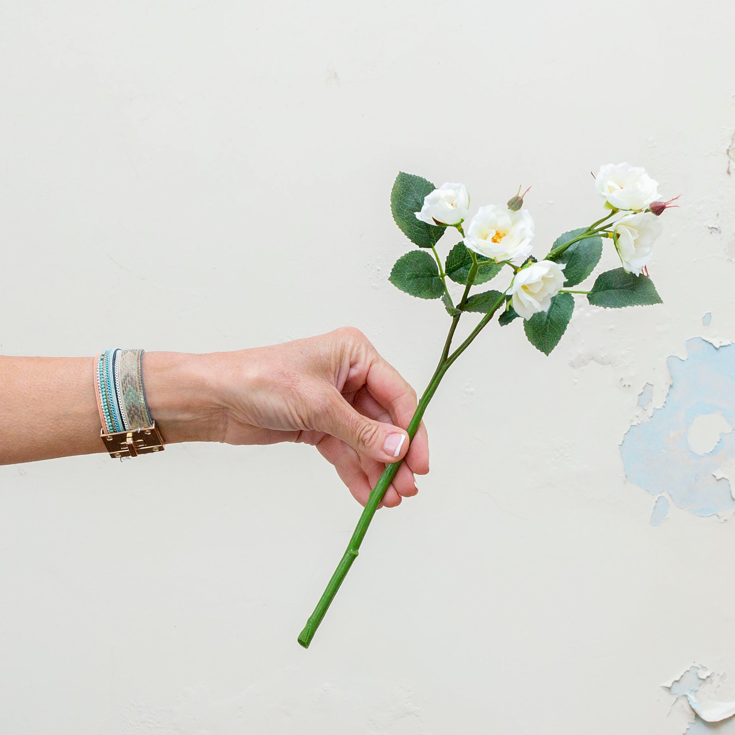 Artificial white rose spray stem being held in hand, featuring multiple open rose blooms and buds with realistic foliage on a natural-look stem